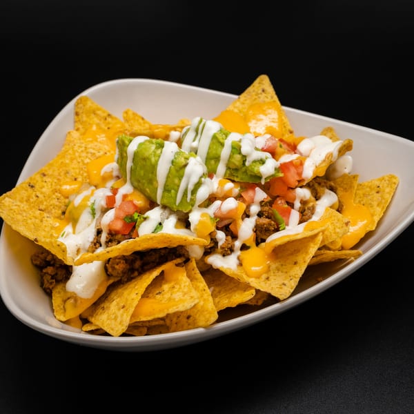 A white bowl of Taco Rey Coliman nachos with ground beef, cheese, guacamole, and sour cream.