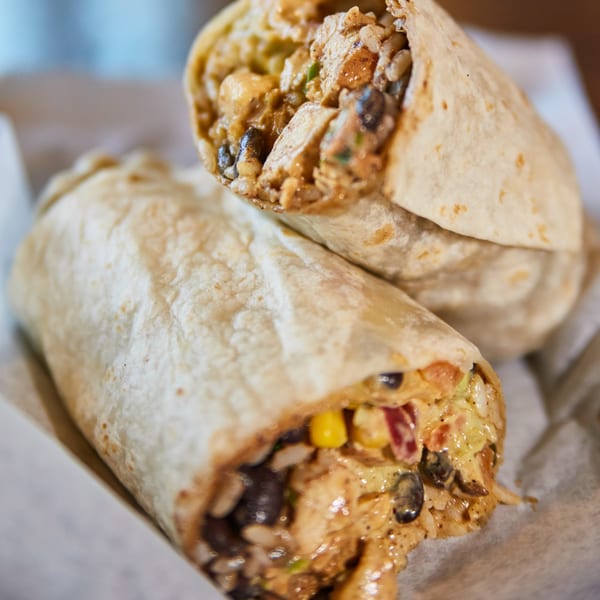 Two large burritos, one cut in half, revealing a hearty filling of chicken, rice, beans, and corn.