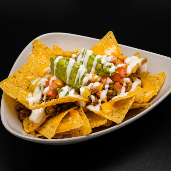 A white bowl of Taco Rey Coliman nachos with cheese, ground beef, guacamole, and sour cream.