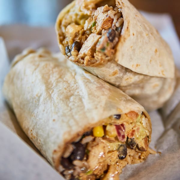 Two large burritos, one cut in half, revealing chicken, rice, beans, and corn inside.